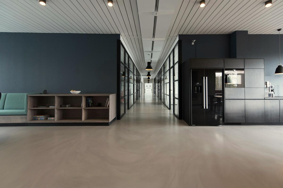 Long couloir de bureaux au sol clair, avec un coin cuisine
