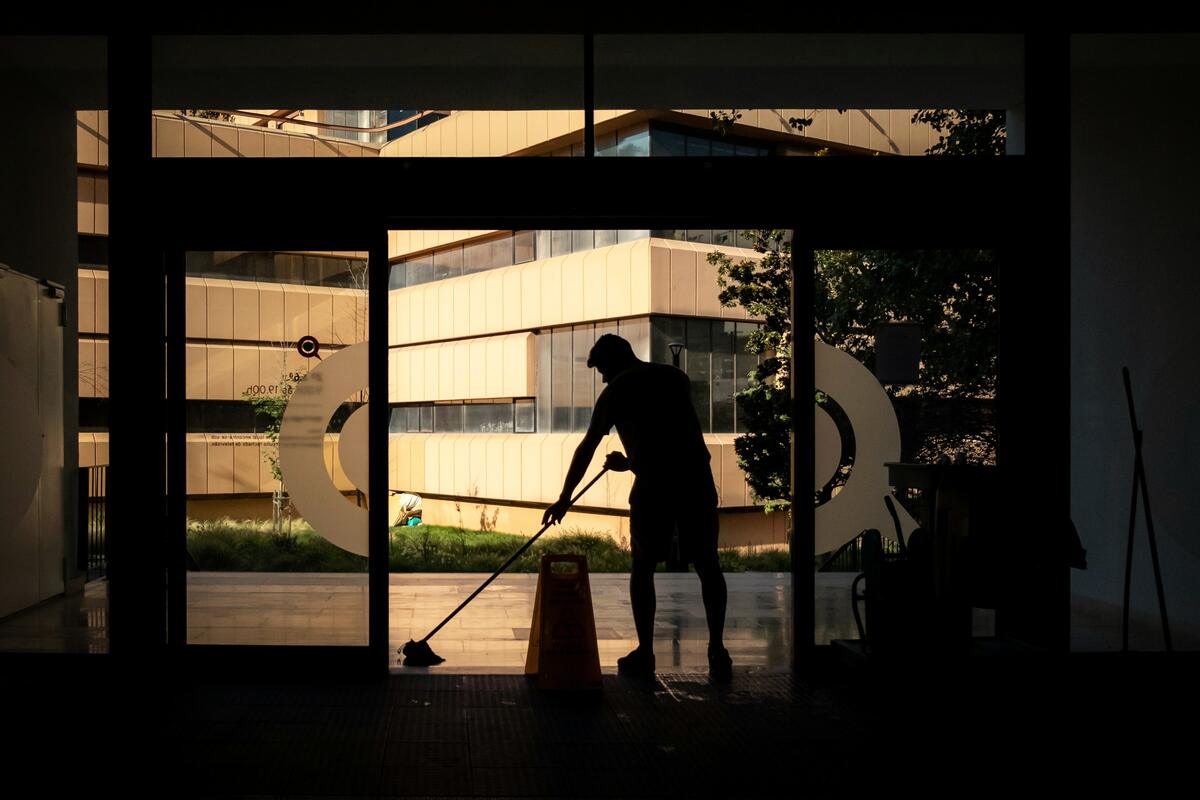 Silhouette d’un agent d’entretien passant la serpillière devant une porte vitrée, en contre-jour